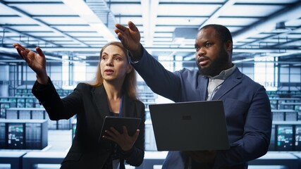 Teamworking technicians managing data center with advanced technology using devices. Coworkers in server room optimizing data center infrastructure with laptop and tablet, camera B