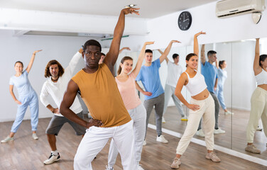 Excited positive diverse men and women of different ages stretching before modern dancing class in school for adults