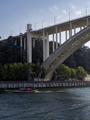 A rabelo boat on the Douro River, passing under the Arrábida Bridge, with the bank on the Vila Nova de Gaia side in the background. Porto, Portugal.