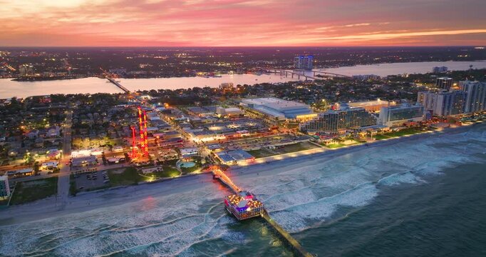 Coastal city of Daytona Beach, Florida with Main Street Pier and Breakers Oceanfront theme park with amusement swings, illuminated luxury hotels at sunset. Tourism infrastructure in southern USA.
