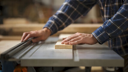 Close-Up of a Woodworker's Hands Carefully Guiding Wood on a Table Saw in a Workshop