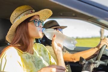 Latina woman drinking water while in a car on her way to enjoy a nice ride. The woman, wearing a...