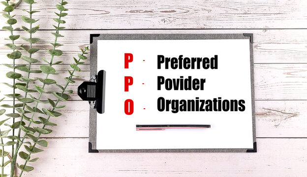 Clipboard with PPO - Preferred Provider Organizations text, pen, and green leaves on wooden table