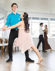 Girl and guy in festive clothes dancing slow ballroom dance during group lesson in a choreography...