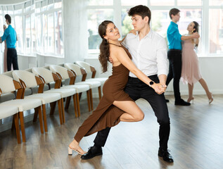Guy and girl in couple spins to rhythm of tango during lesson for novice students. Classes in...