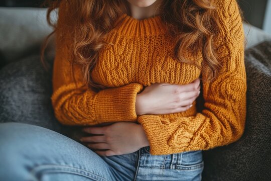 A woman with red hair is sitting on a couch wearing a yellow sweater - Powered by Adobe