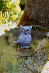 Purple owl statue resting by a tree in a garden, with soft sunlight filtering through leaves