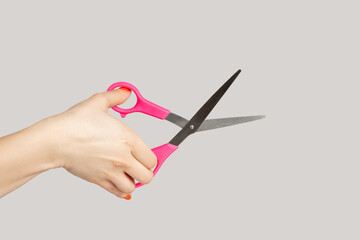 Closeup of woman hand showing hairdresser scissors, equipment for cutting paper, carton, textile. Indoor studio shot isolated on gray background.