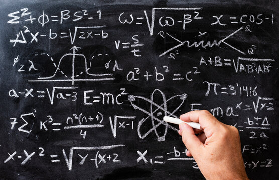 Mano escribiendo operaciones matem&aacute;ticas y formulas de f&iacute;sica cu&aacute;ntica con una tiza en la pizarra