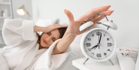 Displeased young woman turning off alarm clock in bedroom, closeup