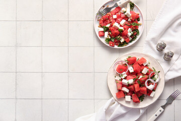 Plates of tasty watermelon salad on white tile background