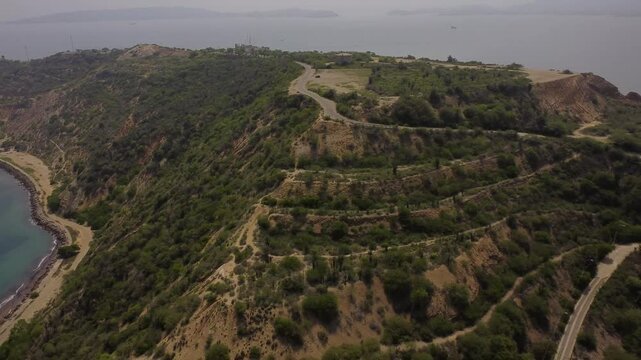Aerial tracking by drone of a compact blue car, rolling on the ridge of a mountain, with arid vegetation and beach in the background