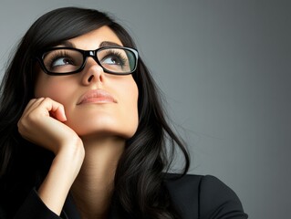 Woman in glasses, thoughtful expression, looking up, gray background.