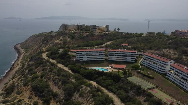 Aerial tracking by drone of a compact blue car, rolling on the ridge of a mountain, with arid vegetation and beach in the background