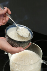 Woman taking boiled rice from pot into bowl, closeup