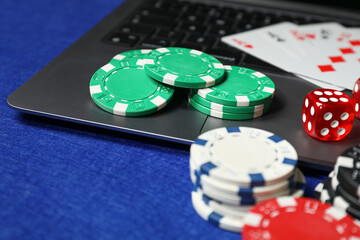 Poker chips, laptop, dice and playing cards on blue table. Online game