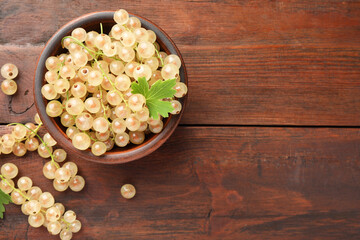 Fresh white currant berries in bowl and green leaf on wooden table, top view. Space for text