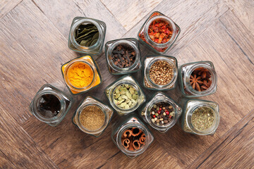 Different spices in glass jars on wooden table, flat lay