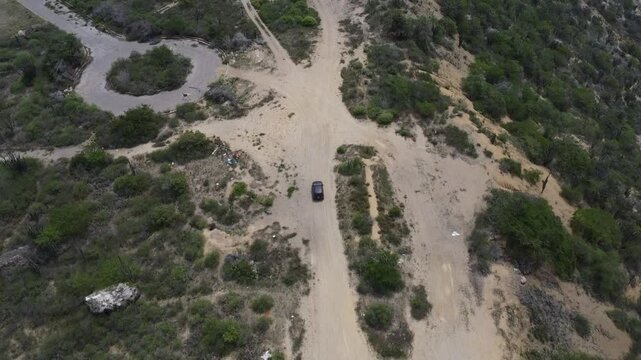 Aerial tracking by drone of a compact blue car, rolling on the ridge of a mountain, with arid vegetation and beach in the background