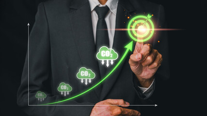 Businessman in a suit pointing at a green graph with CO2 reduction symbols, emphasizing environmental sustainability and carbon footprint reduction.