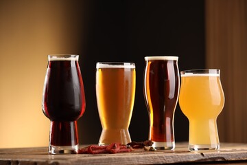 Glasses with different types of beer and snacks on wooden table against color background