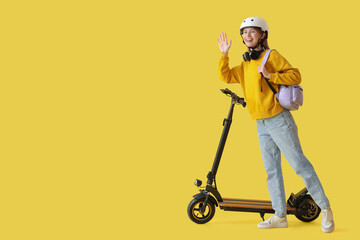 Beautiful young woman in helmet with modern electric kick scooter on yellow background