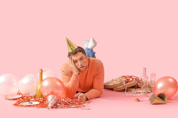 Young man with hangover and balloons lying after Birthday party on pink background