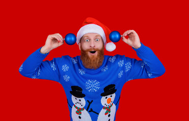 Xmas holiday celebration. Santa man at New Year. Winter holiday for man in Santa hat. Xmas sweater. Man with decoration isolated on red. Merry Christmas. Happy New Year. Welcoming the new year