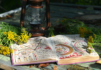 Mystic still life with magic book of spells, old lantern and healing herbs on old table. Occult, esoteric, wicca and divination concept. No foreign language, all symbols are fictional
