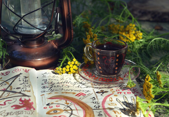 Mystic still life with magic book of spells, cup, old lantern and healing herbs on old table. Occult, esoteric, wicca and divination concept. No foreign language, all symbols are fictional