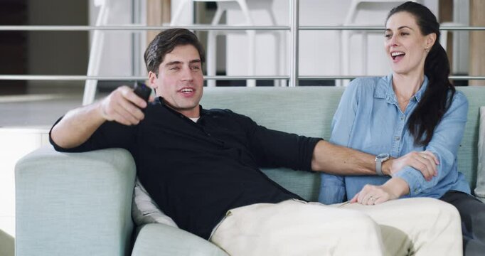 Couple, playful and watching tv on sofa in home for series, movies and streaming service fun. Smile, happy and man teasing woman with television remote in silly, goofy and living room humor in house