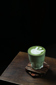 Cup of Matcha Latte With Latte Art on Wooden Table Isolated on Dark Background