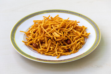Crispy and spicy bhujia snack on a white plate on light wooden surface.