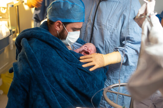 father holding his newborn baby after caesarean section surgery in the hospital operating room, dad doing kangaroo care