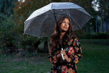 Gorgeous brunette in dress with umbrella pensive, pouring rain, artistic image 