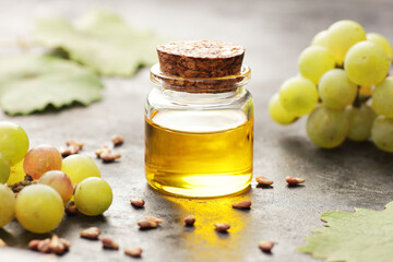 Grape seed oil in glass bottle with grapes, seeds and leaves close on black background, closeup, healthy food and natural skin and body treatment and care concept