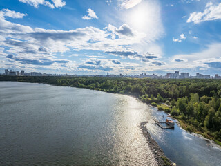 Fototapeta premium Big lake with green shores in bright sun light and city on horizon, aerial landscape. Recreation concept. Aerial view