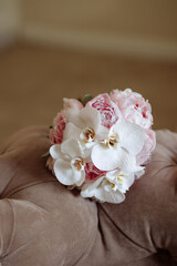 A bouquet of white and pink flowers sits on a brown couch. The flowers are arranged in a way that they look like they are blooming, and the colors of the flowers complement each other