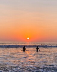 Two people synchronized silhouette walking in ocean during beautiful sunset in san diego california