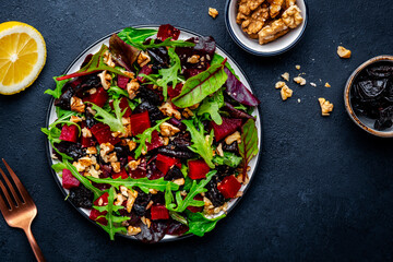 Fresh vegan salad with beetroot, prunes, arugula, chard and walnuts on black background