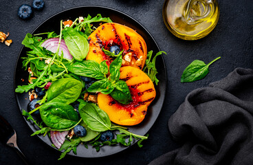 Vegan delicious salad with grilled peaches, fresh blueberries, red onion, walnuts, basil and mixed herbs, black background, top view