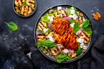 Foodie grill salad with zucchini and chicken, feta cheese, walnuts, red onion and spinach, black background, top view