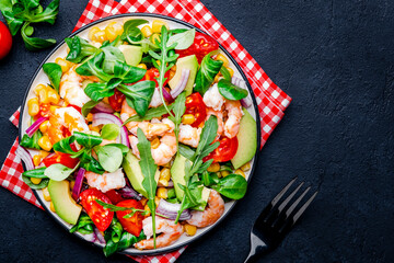 Foodie food salad with shrimps, corn, avocado, tomatoes, lamb lettuce, arugula and red onion on black background. Top  view