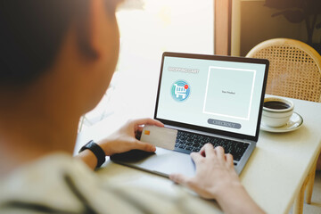 A person completes an online shopping transaction using a laptop and credit card. The screen shows a shopping cart interface, with a checkout option visible, emphasizing e-commerce 