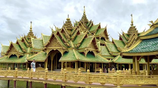 Footage of an asian guy walking on the wood bridge towards Pavilion of the Enlightened, a green temple complex in Muang boran Ancient city, Samut Prakan, Bangkok, Thailand.