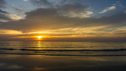 Beautiful sunset above sea or ocean and reflection of sun in the water and sand on beach.