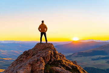 A wanderer stands atop a mountain peak, gazing at a stunning sunset that paints the sky with vibrant hues.