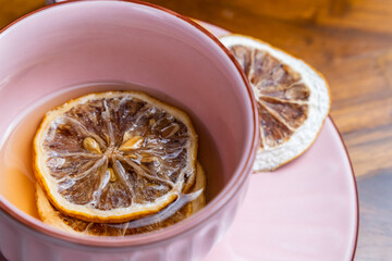 pink color cup of tea with dried lemon slice, on a wooden table
