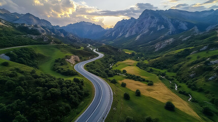 Scenic winding road through lush green valleys and mountains at sunset.
