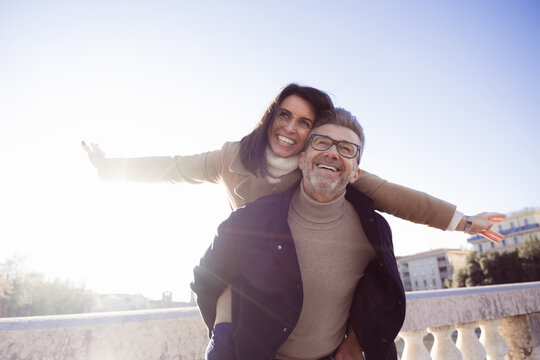 Elated middle-aged couple enjoys a carefree piggyback ride in a city on a sunny winter day